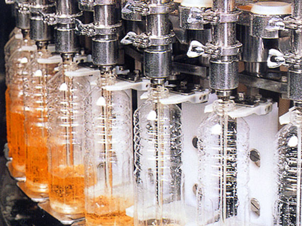 A row of bottles being filled with juice from a machine.